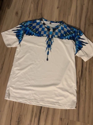 Marcelo burlon tshirt - Vit marcelo burlon tshirt med blåa fågelvingar. Passar perfekt till sommaren!