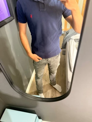 Mörkblå pikétröja från Ralph Lauren - Snygg mörkblå pikétröja från Ralph Lauren med klassisk krage och korta ärmar. Tröjan har den ikoniska röda logotypen broderad på bröstet och är gjord i mjuk bomull. Perfekt till jeans eller shorts för en clean och stilren look.