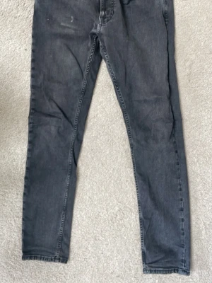 Svarta slim fit jeans från Nudie - Säljer ett par svarta slim fit jeans från Nudie Jeans med klassisk femficksmodell och diskret vågmönster på bakfickan. Jeansen har normal midja och är tillverkade i mjuk denim med lätt tvättad look. Perfekta för en avslappnad och stilren outfit.