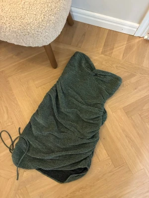 Glittrig grön Adoore klänning - Säljer en glittrig grön axelbandslös kortklänning med snörning i sidan. Klänningen har en figurnära passform och är perfekt för dig som vill sticka ut. Materialet känns mjukt och stretchigt, vilket gör den bekväm att bära hela kvällen. Från Adoore och aldrig använd.