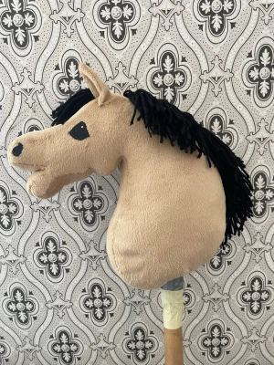 Käpphäst med svart man - Säljer en beige käpphäst med svart man och svans. Hästen har broderade svarta ögon, en vit nosbläs och mjukt tygmaterial. Den är handgjorda. Käppen är av trä och fäst med tejp. Perfekt för lek och fantasi! Den är aldrig använd och man får med vadd💕