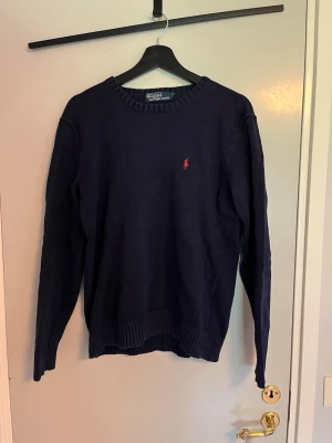 Ralph Lauren tröja - Mörkblå stickad tröja från Polo Ralph Lauren med rund halsringning och klassisk röd broderad logga på bröstet. Tröjan har långa ärmar och ribbade muddar vid ärmslut och nederkant. Perfekt för lager-på-lager och enkel att matcha med jeans. Hör av er vid funderingar mvh Gustav🙌