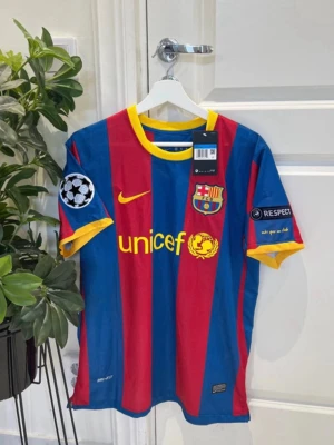 FC Barcelona Messi matchtröja - Säljer en officiell FC Barcelona matchtröja från Nike med Messi 10 på ryggen. Tröjan har blå och röda vertikala ränder, gula detaljer vid krage och ärmslut samt Champions League-märken på ärmarna. Unicef-logga på framsidan och klubbmärke på bröstet.