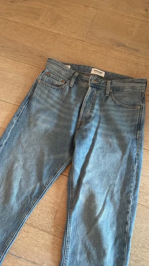 Blå raka jeans från Jack and Jones  - Säljer ett par klassiska blå jeans från Jackandjones med rak passform och femficksdesign. Jeansen har en ljusblå tvätt och är tillverkade i denim. Perfekta för dig som gillar en enkel och tidlös look. Modell: relaxed chris. 29/30.