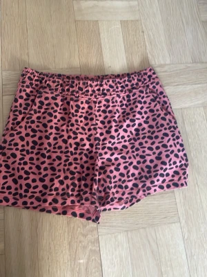 Rosa leopardmönstrade shorts - Snygga rosa shorts med svart leopardmönster och elastisk midja. Perfekta för varma dagar och ger en cool vibe till din outfit. Mjukt material som känns skönt mot huden.