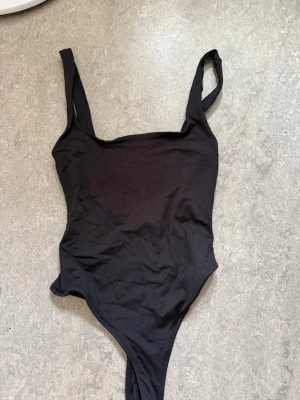 Svart ribbad body med breda axelband - En enkel och stilren svart body med breda axelband och fyrkantig urringning från Zara. Aldrig använt. Jättemjukt och skönt material.