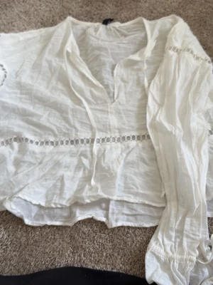Vit boho-blus med spetsdetaljer - Säljer en luftig vit blus i boho-stil med långa ärmar och dekorativa spetsdetaljer. Blusen har v-ringning och snörning vid ärmsluten för extra stil. Perfekt till jeans eller kjol för en avslappnad look.