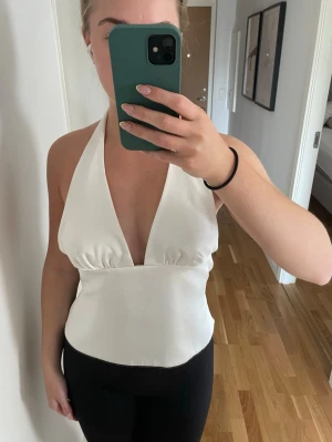 Vit halterneck topp från Zara - Säljer en vit halterneck topp med djup urringning och öppen rygg. Satin liknande material 