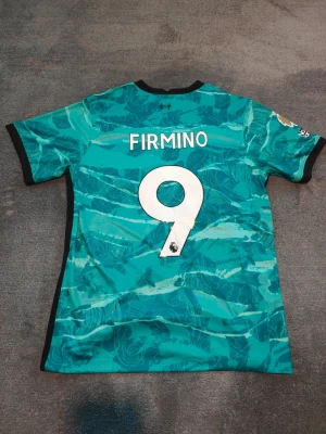 Liverpool Bortatröja | 2020-21 | Firmino - Liverpools bortatröja från säsongen 2020-21. Firmino, nr 9 på ryggen. Stadium/fan edition. Ny & oanvänd. Storlek large. Tröjan är en replika i utmärkt kvalitet. Skickas 1-3 dagar efter mottagen betalning. Har du frågor/funderingar är det bara att höra av dig! :)