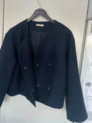 Mörkblå kappa från Gino Tricot - Stilren mörkblå kappa från Gino Tricot med minimalistisk design och dubbelknäppning framtill. Rak passform, rundad halsringning och helfodrad insida. Perfekt för dig som gillar klassiska och tidlösa plagg.