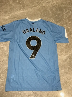 Manchester City Haaland matchtröja - Snygg ljusblå Manchester City matchtröja från Puma med Haaland och nummer 9 på ryggen. Tröjan har klubbmärke, sponsortryck och svarta detaljer. Tillverkad i lätt och ventilerande material, perfekt för fotboll eller träning. 