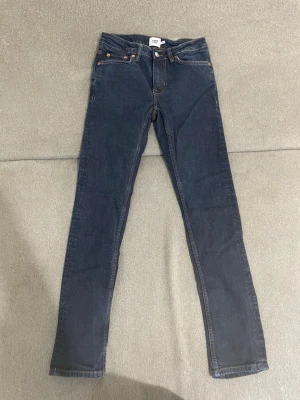 Mörkblå skinny jeans från 157 - Snygga mörkblå skinny jeans från 157 med klassisk femficksdesign och kontrastsömmar. Jeansen har knappgylf och nitar i kopparfärg. Perfekta för dig som gillar en enkel och stilren look.