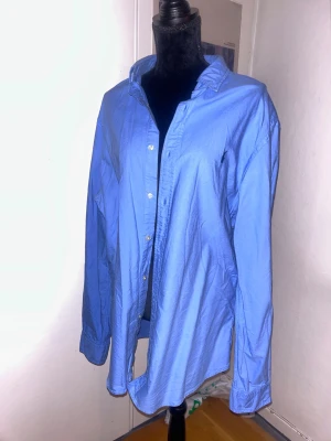 Blå skjorta från Ralph Lauren XL - Klassisk blå skjorta från Ralph Lauren i slim fit-modell. Skjortan har långa ärmar, knappar framtill och en tidlös krage. Tillverkad i mjuk bomull som känns skön mot huden. Perfekt för dig som gillar en clean och stilren look.