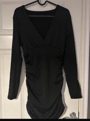 Svart figurnära klänning med djup v-ringning - Snygg svart kort klänning med lång ärm och djup v-ringning. Figurnära passform med lätt rynkade detaljer längs sidorna En tidlös must-have i garderoben passar lika bra till fest som middag eller utekväll🖤(har även sytt där fram vid brösten för den var lite för urringad för min smak går att ta bort om man vill inget som direkt syns, ifrån shein)