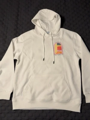 Vit hoodie från Casablanca - Snygg vit hoodie från Casablanca med färgglad grafisk print fram och stort tryck på ryggen. Klassisk känguruficka och dragsko i huvan. Tillverkad i mjukt bomullsmaterial för skön känsla. Perfekt för dig som gillar streetwear och unika prints. STORLEK M, PASSAR S-M. HELT NY.