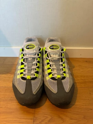 Nike Air Max 95 Neon skor  - Nike Air Max 95 sneakers i grått, svart och vitt med neon-gula detaljer. Skorna har mesh- och mockapaneler, synlig Air Max-dämpning i sulan och klassisk snörning. Ikonisk retrostil som sticker ut med sina färgblock och coola detaljer.