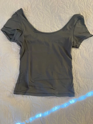 Grå croppad topp med kort ärm - Snygg grå topp med croppad passform och korta ärmar. Djup, rundad urringning framtill ger en trendig look. Perfekt att matcha med höga jeans eller kjol för en stilren outfit.