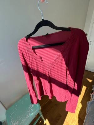 Vinröd spetsdetaljerad topp Gina Tricot - Vinröd långärmad topp från Gina Tricot med v-ringning och spetsdetaljer längs halsringningen. Tunn och mjuk i materialet, perfekt för lager på lager eller som den är. Enkel men ändå söt design som passar till mycket🥂