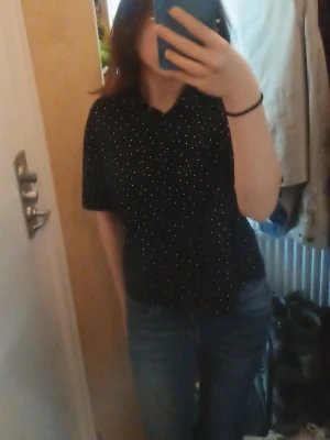 Svart prickig skjorta med kort ärm - Snygg svart skjorta med vita prickar och korta ärmar. Skjortan har klassisk krage och knappar framtill. Perfekt till jeans eller kjol för en chill och stilren look.