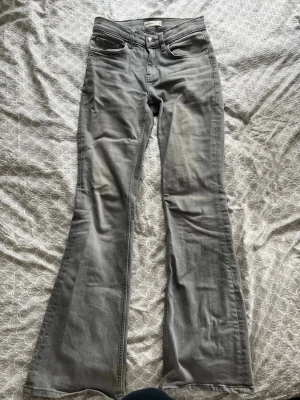Gråa bootcut jeans från Gina Tricot - Säljer ett par gråa bootcut jeans från Gina Tricot. Jeansen har klassisk femficksmodell, hög midja och utsvängda ben. Tillverkade i mjukt denimtyg med lätt tvättad look. Perfekta för dig som gillar retrostil och vill ha ett par snygga jeans med skön passform.