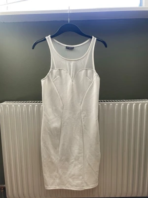 Vit ärmlös klänning Sally Circle - Säljer en vit, ärmlös klänning från Sally Circle. Klänningen har en kroppsnära passform och mesh-detaljer upptill vid halsringningen. Perfekt för dig som gillar stilrena och moderna plagg med en twist. Eller en klänning till din student 👩‍🎓 