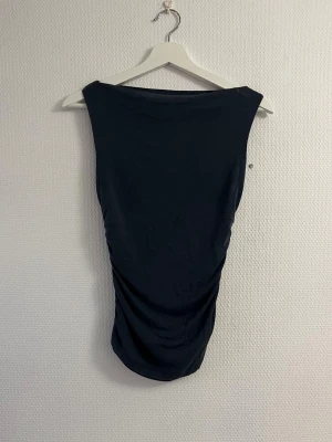 Svart ärmlös linnetopp - Säljer en svart, tight och ärmlös linnetopp med rund halsringning. Toppen har en enkel och stilren design utan synliga detaljer eller mönster, vilket gör den lätt att matcha med olika outfits. Perfekt för dig som gillar minimalistisk stil.