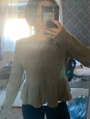 Brun peplumkofta med knappar - Säljer en  kofta med peplumvolang och rund halsringning. Koftan har långa ärmar och knäpps framtill med matchande knappar. Perfekt för dig som gillar en feminin och stilren look.