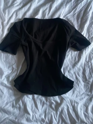 Svart kortärmad topp med rund hals - En enkel och stilren svart topp med rundad halsringning och korta ärmar. Toppen har en figurnära passform och är tillverkad i ett mjukt, stretchigt material som känns bekvämt mot huden. Perfekt att matcha med jeans eller yogapants.