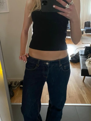 Mörkblå low waist jeans - Säljer ett par mörkblå low waist jeans med raka ben och klassisk femficksdesign. Jeansen har kontrastsömmar och silverfärgad knapp. Perfekta för en avslappnad och trendig look. Materialet är denim i bomull.