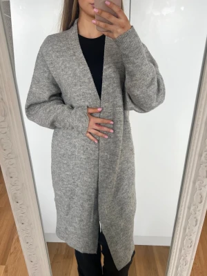 Kofta - Lång, öppen grå kofta med beiga inslag i mjuk stickad kvalitet. Koftan har långa ärmar, ribbade muddar och en avslappnad passform. Supermysig 💕 Storlek XS från H&M. Lite nopprig men har mer att ge. 