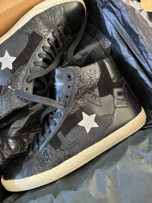 Saint Laurent svarta high top sneakers - Svarta high top sneakers från Saint Laurent med stjärndetaljer i vitt och glitter, svart mocka och läderpaneler samt vita sulor. Snygga kontraster mellan material och coola detaljer som ger en unik vibe.