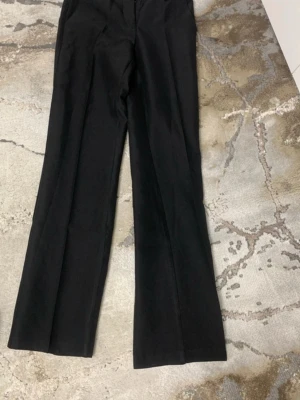 Svarta kostymbyxor  - Säljer ett par klassiska svarta kostymbyxor från Nelly. Byxorna har raka ben, hällor för skärp och diskreta sidofickor. Perfekta för en clean och stilren look. Materialet känns mjukt och har en lätt stretch för extra komfort.