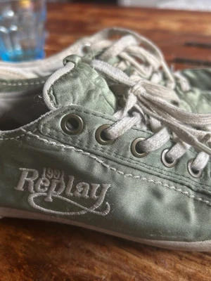 Replay gröna låga sneakers - Snygga låga sneakers från Replay i en ljusgrön nyans med vita detaljer och snörning. Skorna har metallfärgade öljetter och är tillverkade i textilmaterial med broderad logga på sidan. Perfekta för en avslappnad och trendig stil.