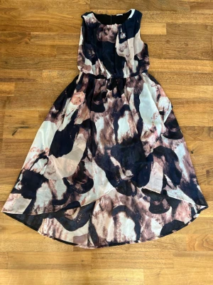 Mönstrad långklänning  - Säljer en flowy långklänning med abstrakt mönster i marinblått, beige och ljusrosa toner. Klänningen har ärmlös design, rund halsringning och ett lätt transparent material som ger en luftig känsla. Perfekt för sommarens alla tillfällen!