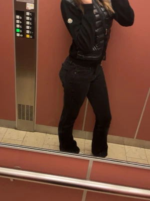  Moncler cardigan - Snygg svart dunväst från Moncler med glansig finish och dragkedja framtill. Västen har en kort, figurnära passform och Moncler-logga på bröstet. Perfekt att slänga över en hoodie eller tröja för en trendig lager-på-lager-look.