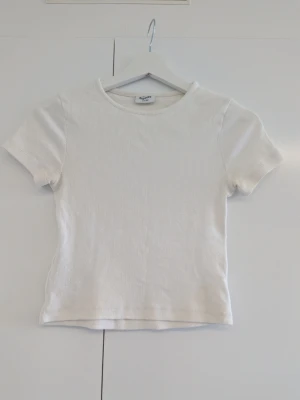 Vit ribbad t-shirt från KappAhl  - En enkel och stilren vit ribbad t-shirt från KappAhl. Mjukt material som är stretchigt och snygg att matcha till en kjol eller jeans. Storlek 158 - 164.
