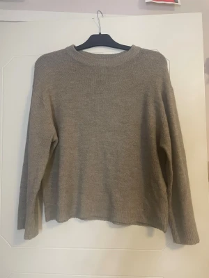 Beige stickad tröja från 157 - Mysig beige stickad tröja från 157 med rund halsringning och långa ärmar. Tröjan har en enkel och avslappnad passform med ribbstickade muddar vid hals, ärmslut och nederkant. Perfekt för lager på lager under kyliga dagar.