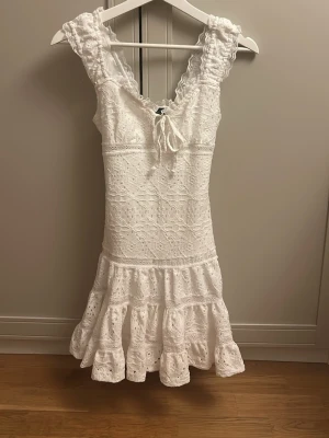Vit spetsklänning med volang - Superfin vit klänning med breda axelband, v-ringning och knyt fram. Klänningen har vackra spetsdetaljer och volangkant nertill som ger en romantisk känsla. Perfekt för sommarens alla tillfällen! Passar mig som bär xs