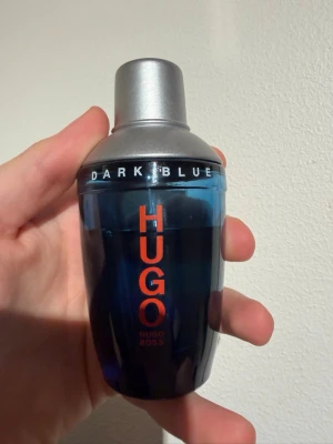Hugo Boss Dark Blue Eau de Toilette - Hugo Boss Dark Blue Eau de Toilette i en cool blå glasflaska med silverfärgat lock. Flaskan rymmer 75 ml och har en modern, stilren design med orange text. Tillverkad i Tyskland och perfekt för dig som gillar fräscha och maskulina dofter. Cirka 50ml kvar.