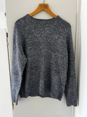 Grå stickad tröja - En stilren, grå stickad tröja med rund hals och långa ärmar. Tröjan har en avslappnad passform och ribbstickade muddar vid ärmslut och nederkant. Perfekt för lager på lager och enkel att matcha med olika outfits.