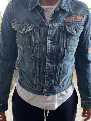 Kaporal jeansjacka med patchar - Snygg blå jeansjacka från Kaporal med flera broderade patchar och detaljer på bröstet och ärmen. Klassisk modell med knappstängning, två bröstfickor med lock och dekorativa sömmar. Perfekt för dig som vill ha en unik och trendig denimlook.