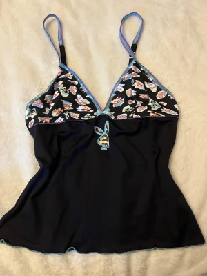 Svart Playboy nattlinne med blommigt mönster - Sött svart nattlinne från Playboy med blommigt mönster på bysten och blå detaljer. Justerbara axelband och en liten kanindekor.