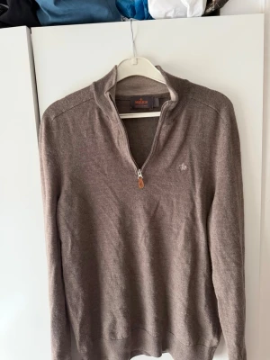 Beige stickad tröja från Morris - Säljer en beige stickad tröja från Morris i 100% merinoull. Tröjan har halv dragkedja framtill, ribbade muddar och en liten broderad logga på bröstet. Perfekt för dig som gillar klassisk och stilren design.