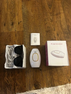 IPL laser hårborttagningsapparat - IPL laser hårborttagningsapparat i vitt med gulddetaljer. Kommer med skyddsglasögon, laddningssladd och manual. Perfekt för enkel och smidig hårborttagning hemma. Modern design och lätt att använda. Använd på ena armen en gång. Köpt på silkyskin för 799