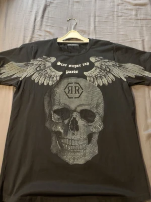 Svart t-shirt från Semple&Man - Cool svart t-shirt från Semple&Man med tryck av stora grå vingar över axlarna och texten 'Star super top paris' på bröstet. T-shirten har rund hals och är kortärmad, perfekt för en avslappnad streetstyle-look.