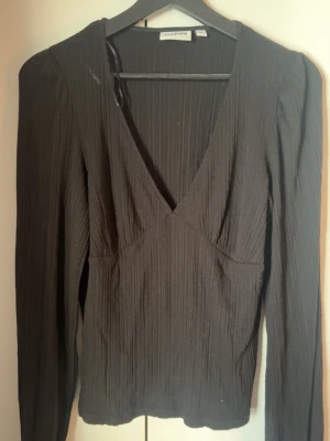 Svart ribbad topp  - Snygg svart långärmad topp från Kappahl med djup v-ringning och ribbad struktur. Toppen har en figurnära passform och är perfekt för att lyfta vilken outfit som helst. Tillverkad i mjukt och stretchigt material! aldrig använd❤️
