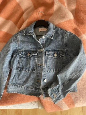 Blå jeansjacka från Nelly XS - Snygg blå jeansjacka från, med en rak passform, krage och långa ärmar. Perfekt att slänga över en hoodie eller t-shirt. Jackan är använd ett fåtal gånger och är nytvättad! Har inga tecken på användning och o superbra skick. Köpt för 599 förra sommaren.