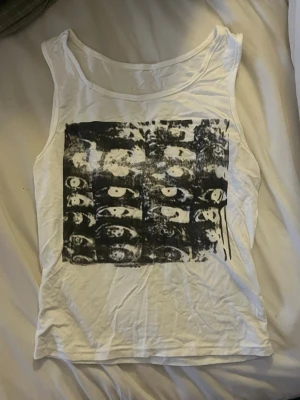 Vit linnetopp med svart tryck - Säljer en vit top (linne) med grafiskt tryck. Varan är inte stryckt på dessa bilder )därför så ser den skrynklig ut) Toppen har rund halsringning.