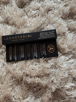 Anastasia Brow Wiz Medium Brown - Slim ögonbrynspenna från Anastasia Beverly Hills i färgen Medium Brown. Pennan har en tunn spets för exakt applicering och en spoolie-borste för att forma brynen. 