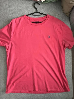 Röd t-shirt från Polo Ralph Lauren - Säljer en röd t-shirt från Polo Ralph Lauren med klassisk passform och rund hals. T-shirten har korta ärmar och den ikoniska lilla loggan broderad på bröstet. Tillverkad i mjuk bomull som är skön att bära hela dagen.